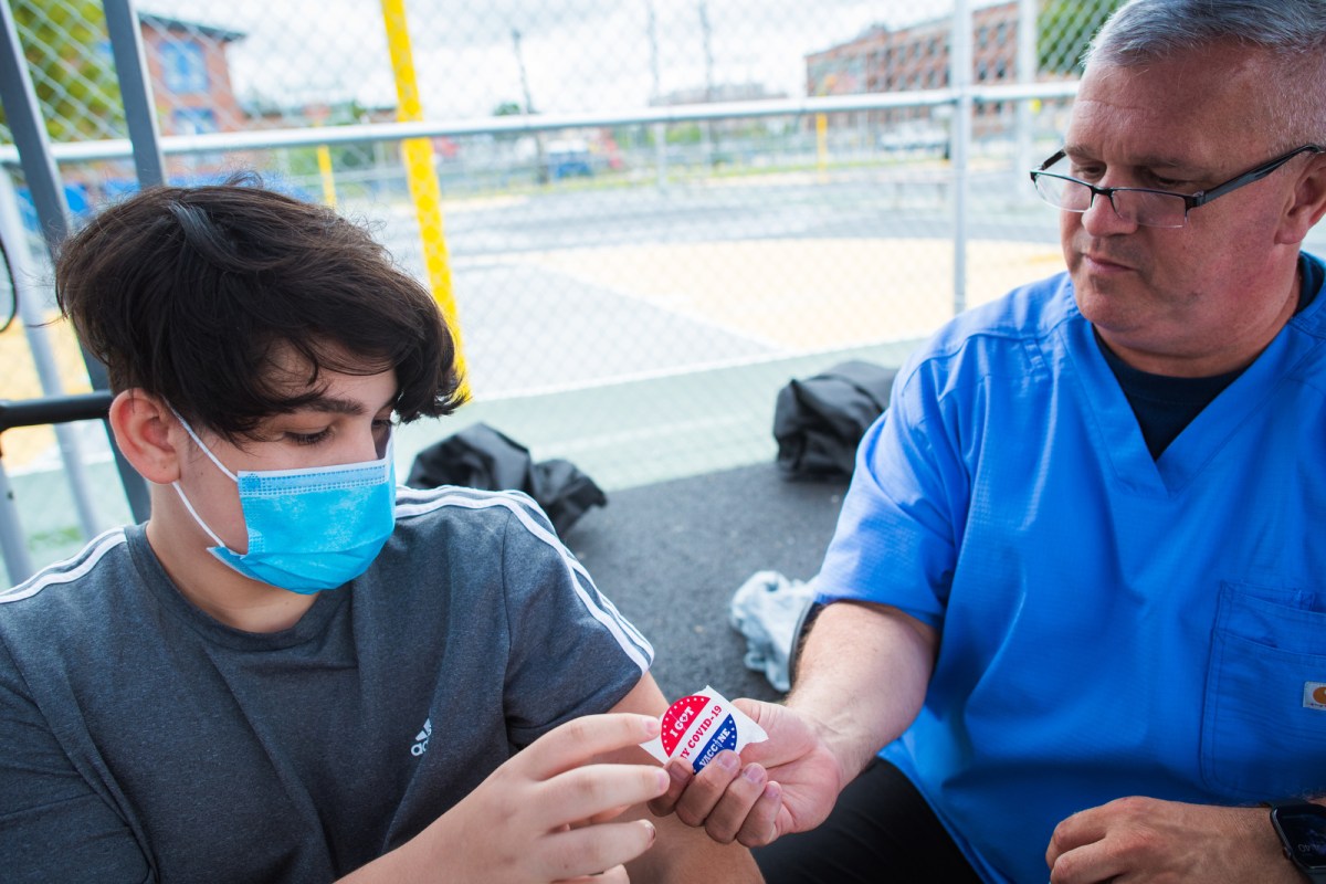 John Pizzo, a public health nurse for the Rhode Island National Guard hands a sticker to Victor Urizar, 15, of Providence after giving him a COVID-19 vaccine at Bucklin Park in August.
