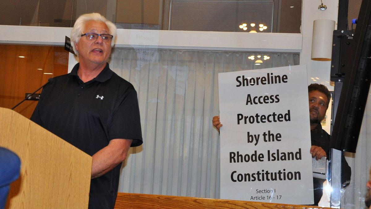 Shoreline access advocate Steve Cersosimo speaks at a recent meeting of the Westerly Town Council, as another advocate, Conrad Ferla, holds a sign publicizing shoreline rights guaranteed under the Rhode Island Constitution.