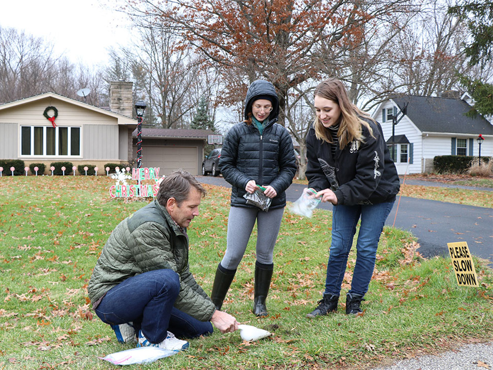Researchers collect a soil sample in the lawn of a house.