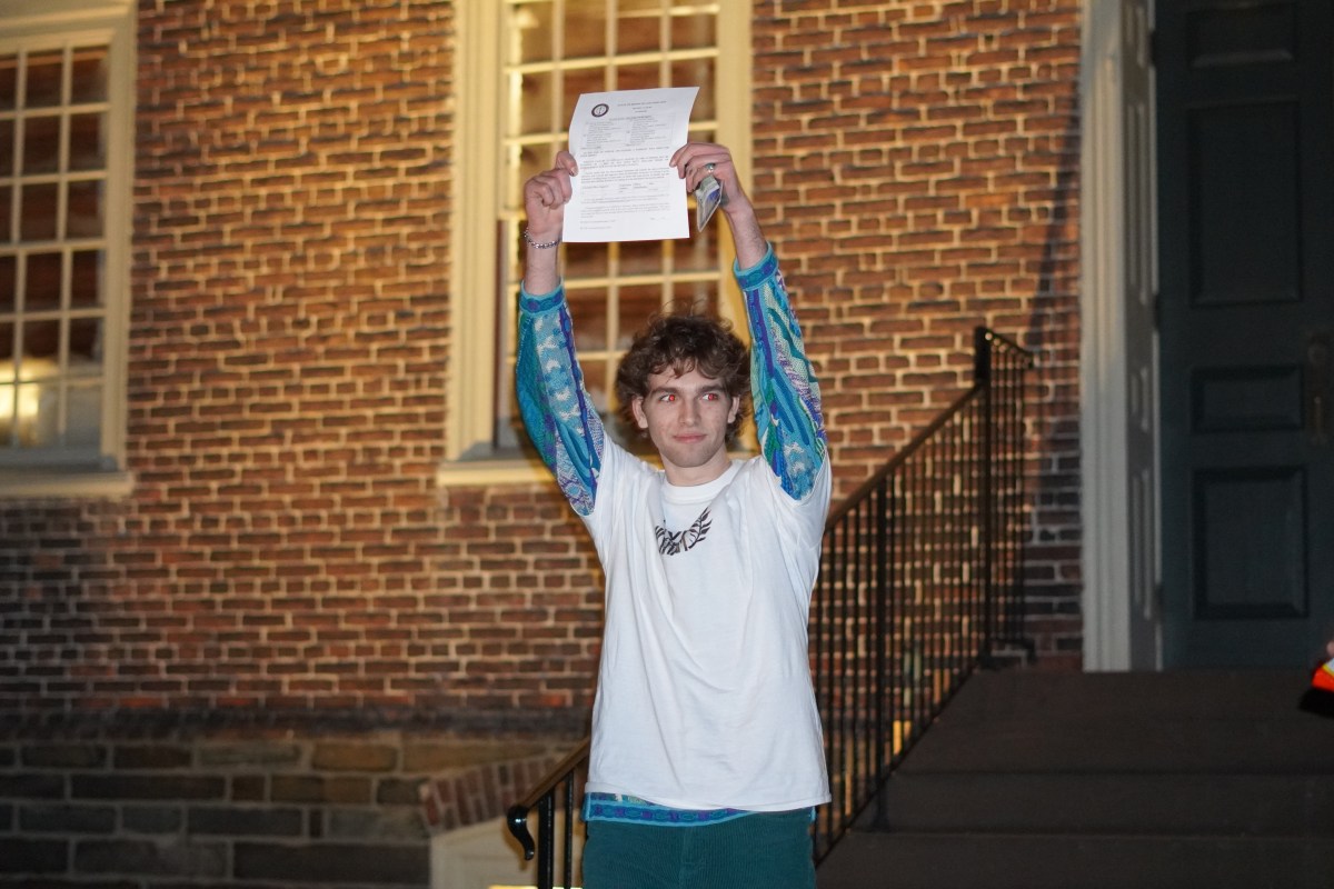 A student walks out of a college building at night after being arrested on trespassing charges. He is valiantly holding up charging documents.