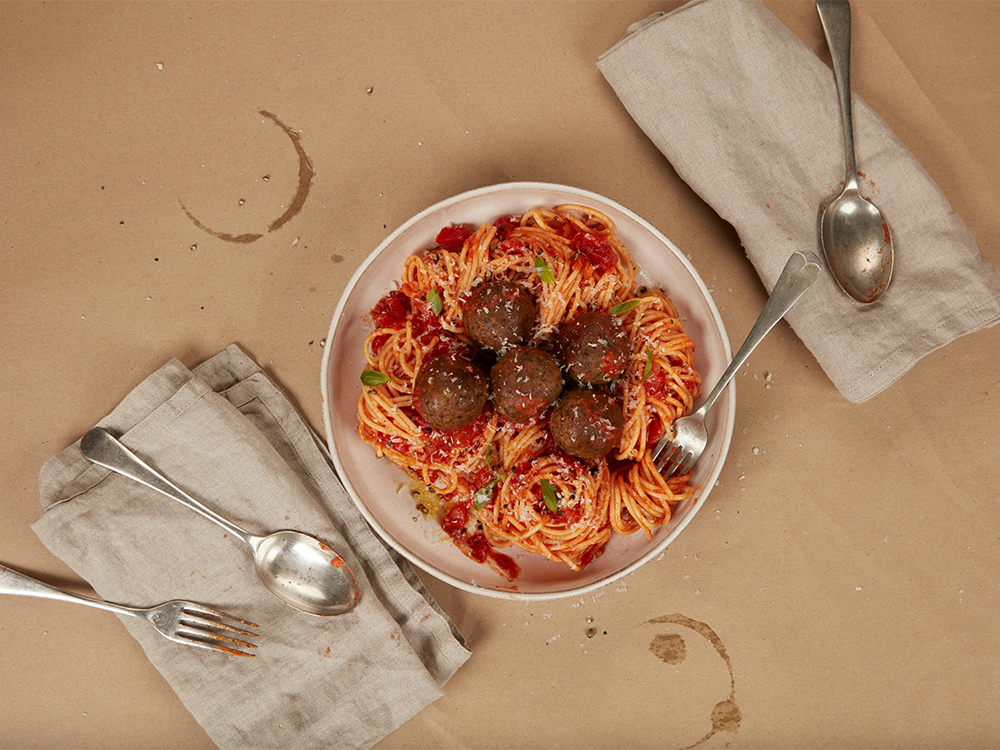 A photo of spaghetti and meatballs on a plate with napkins and silverware beside the plate.