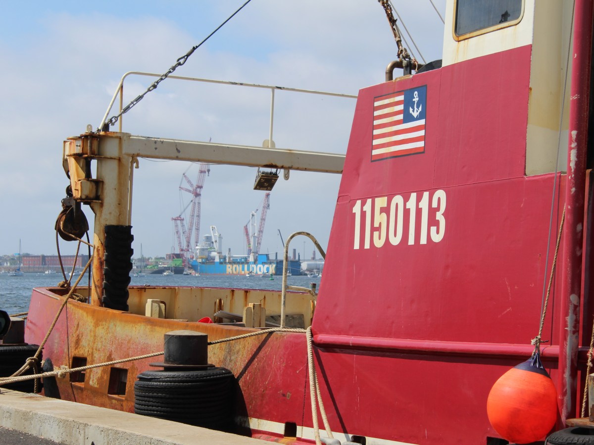 A view of offshore wind construction work through iron scaffolding of a fishing boat.