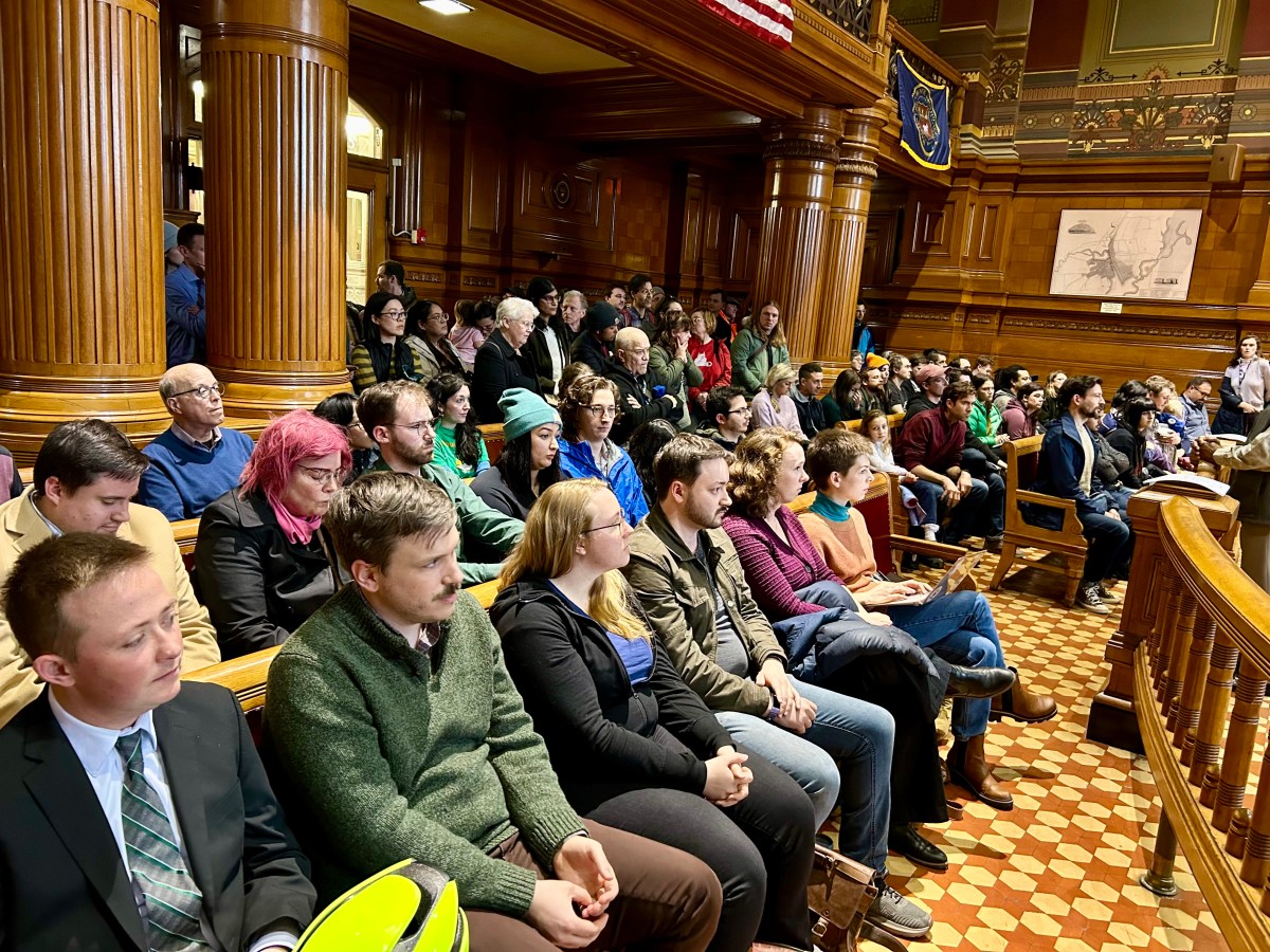 Dozens of people sit shoulder to shoulder in city council chambers