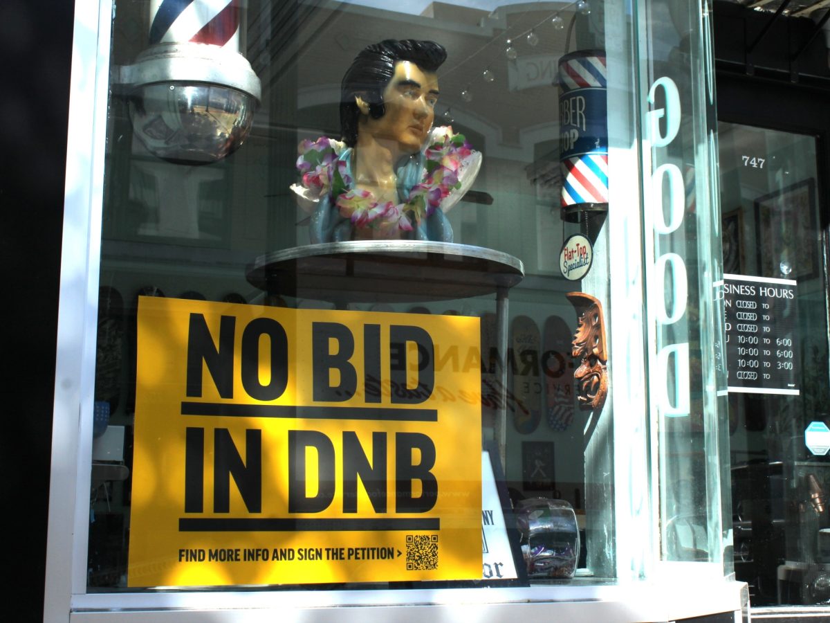 A bright yellow sign opposing the business improvement district hangs in the window of the Stepping Razor, a barber shop.