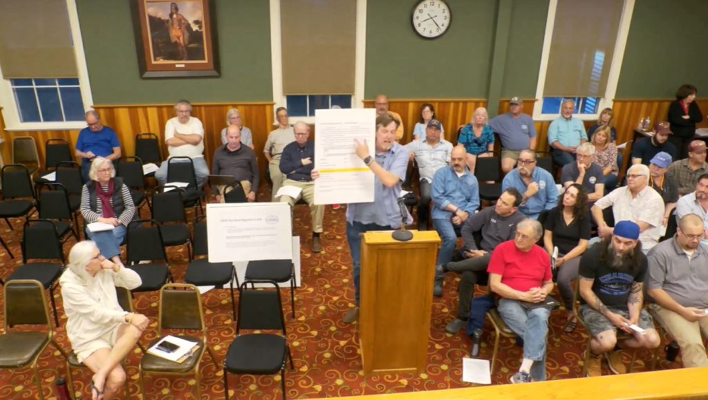 Nope’s Island Conservation Association President Michael Sands, center, speaks at a recent meeting of the Charlestown Town Council. Pictured left of the sign, Deming Sherman, former legal counsel to the Weekapaug Fire District and Nope’s Island Conservation Association, who also spoke in favor of a proposal to further restrict vehicle use on the Quonochontaug Barrier Beach.