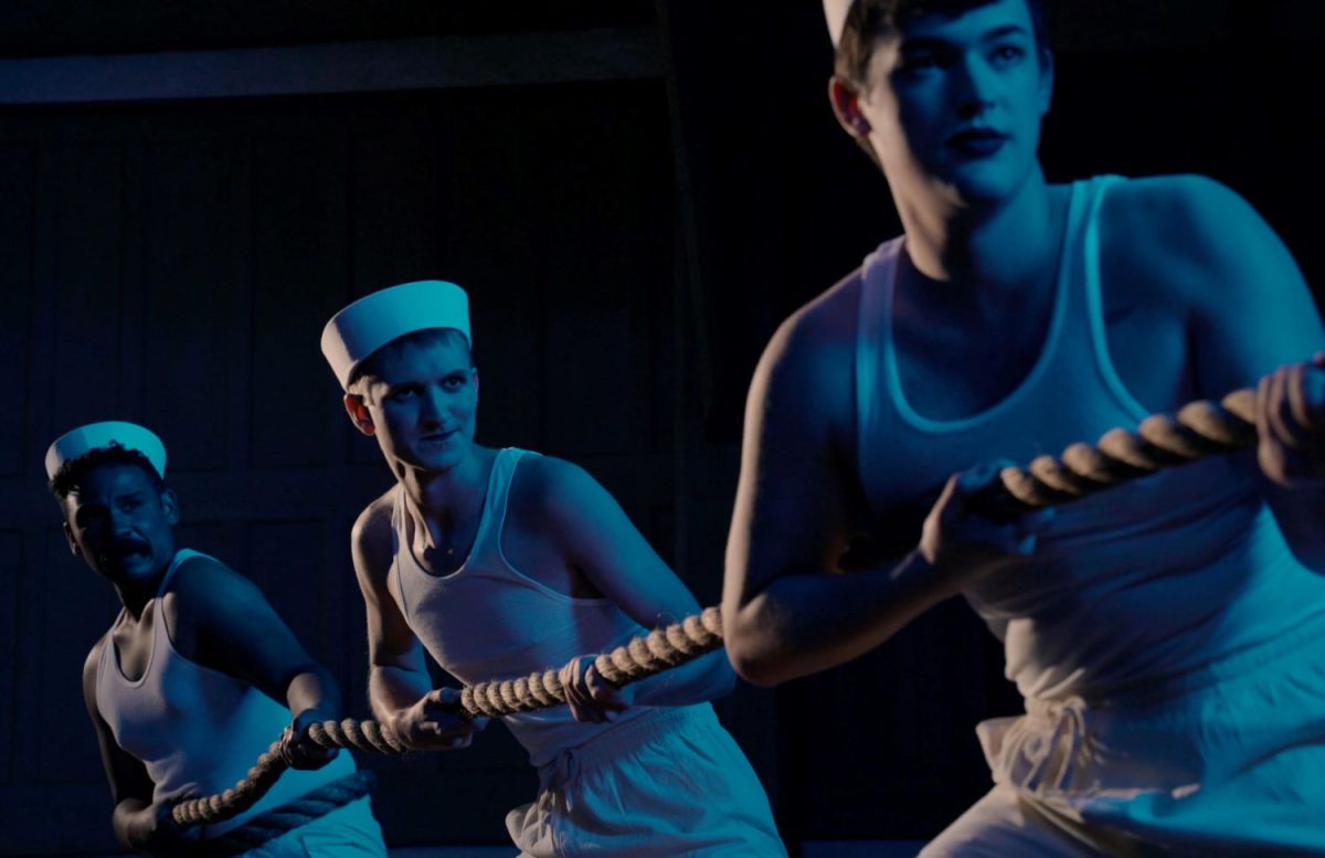 Three sailors in white caps and A-frame shirts pull on a rope.