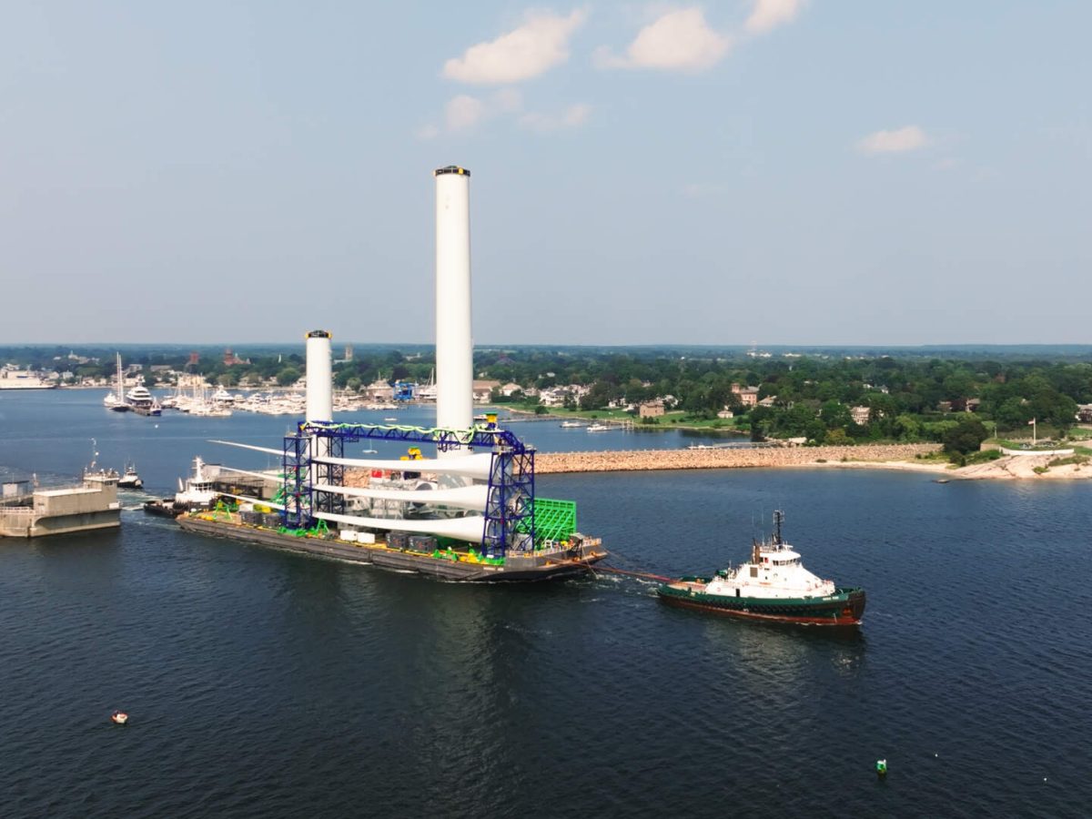 A tug boat pulls a barge carrying offshore wind blades out of New Bedford's harbor.